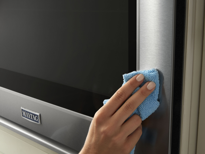 Person wiping stainless steel Maytag® appliance