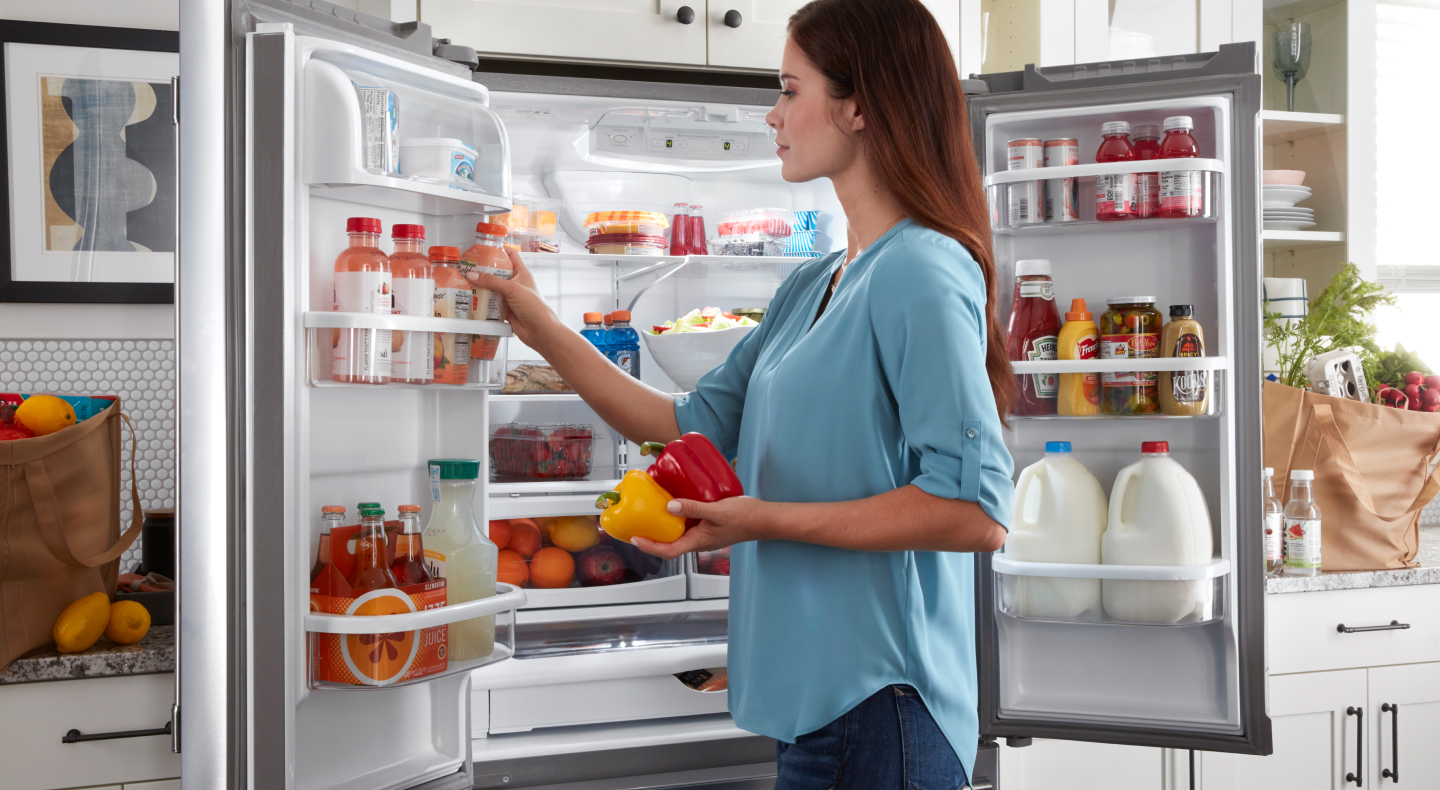 Person standing at an open fridge putting produce away