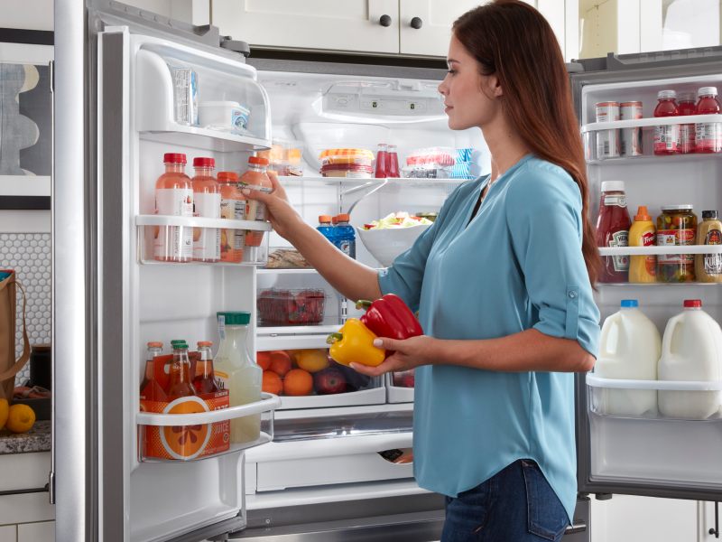 Person standing at an open fridge putting produce away