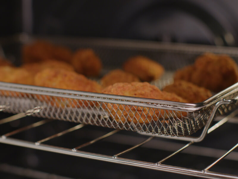 Chicken strips cooking in an air fryer basket
