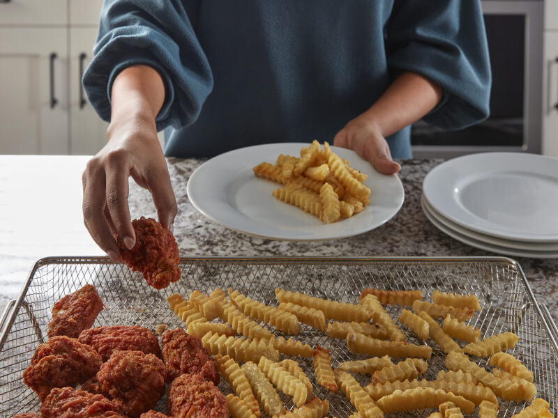 Person filling an air fry basket with chicken strips and fries