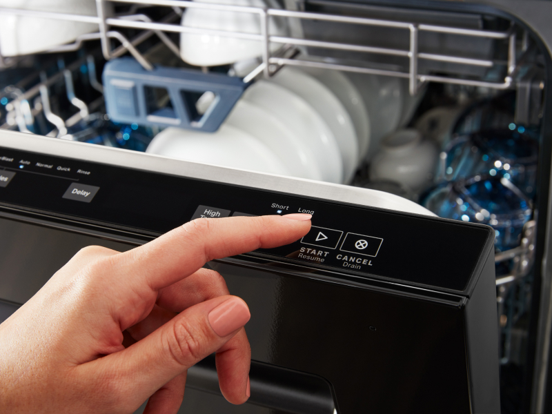 Person selecting start button on a top control dishwasher