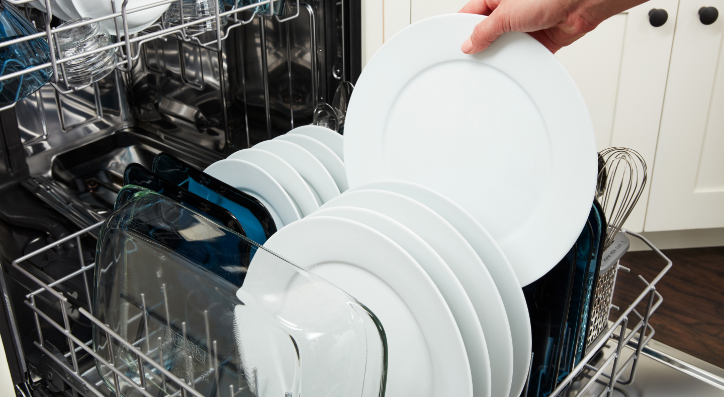 Person unloading plates from the bottom rack of a dishwasher