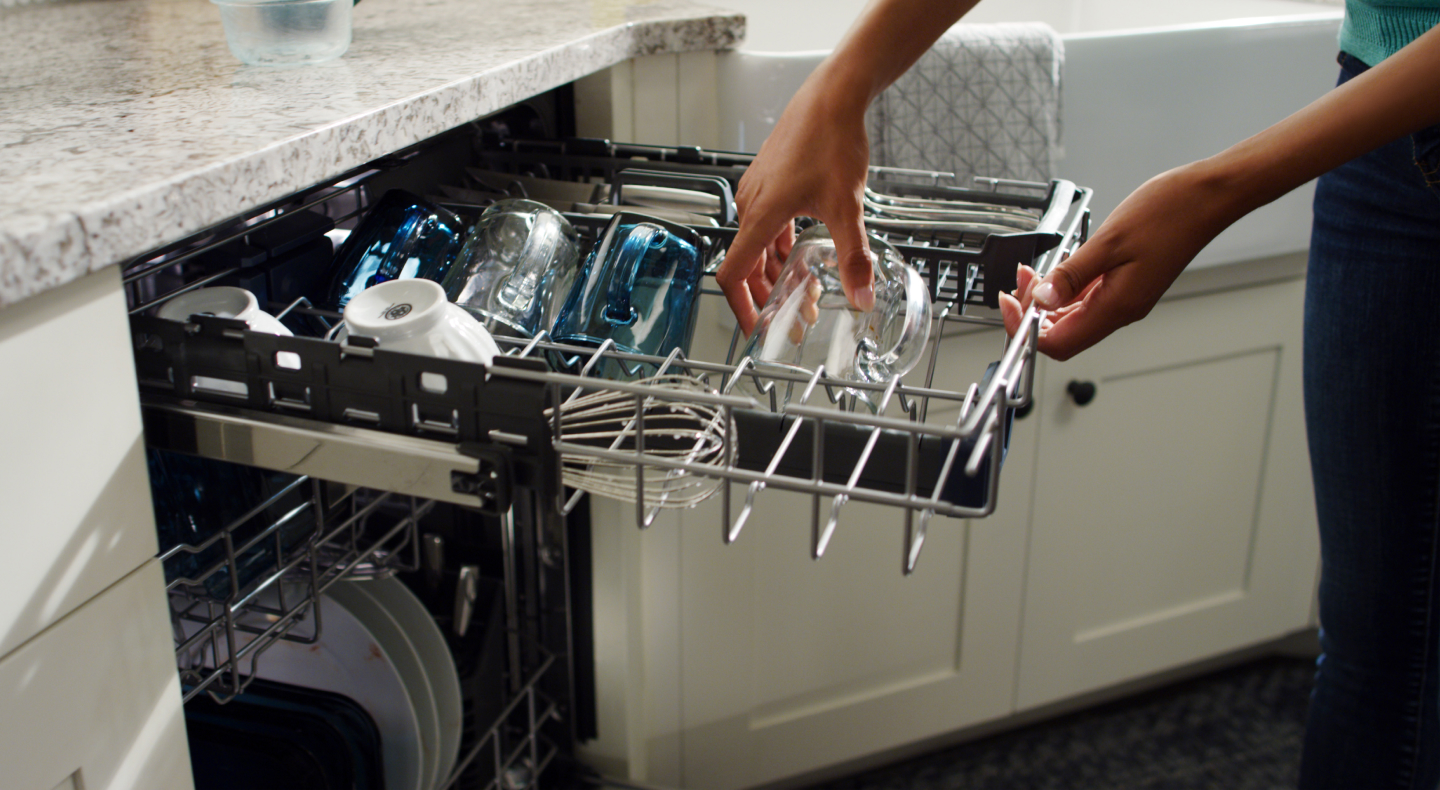 Person loading a glass into a third rack of a dishwasher