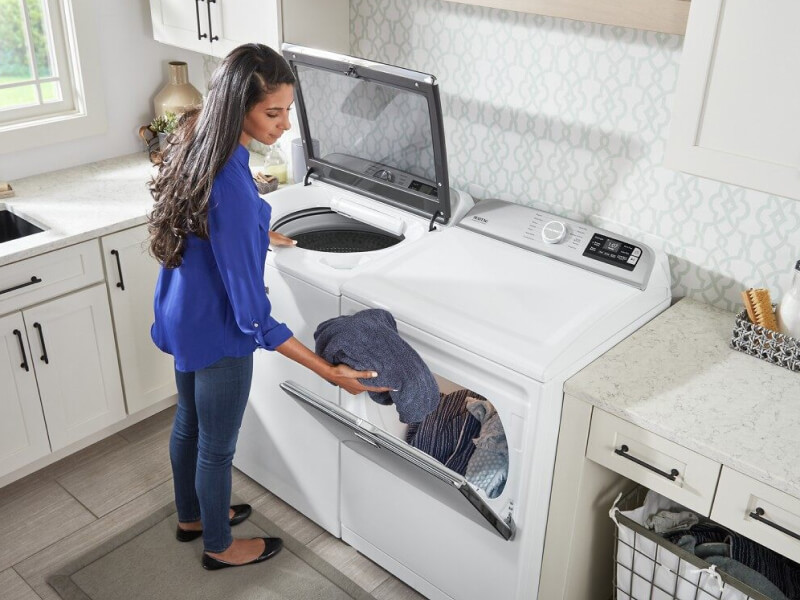 A woman loading washed laundry into a dryer