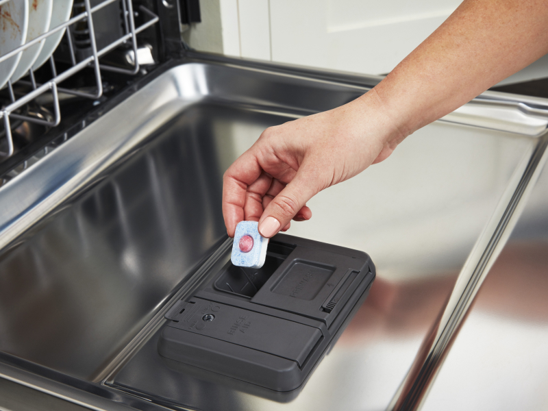 Person placing tablet in dishwasher dispenser