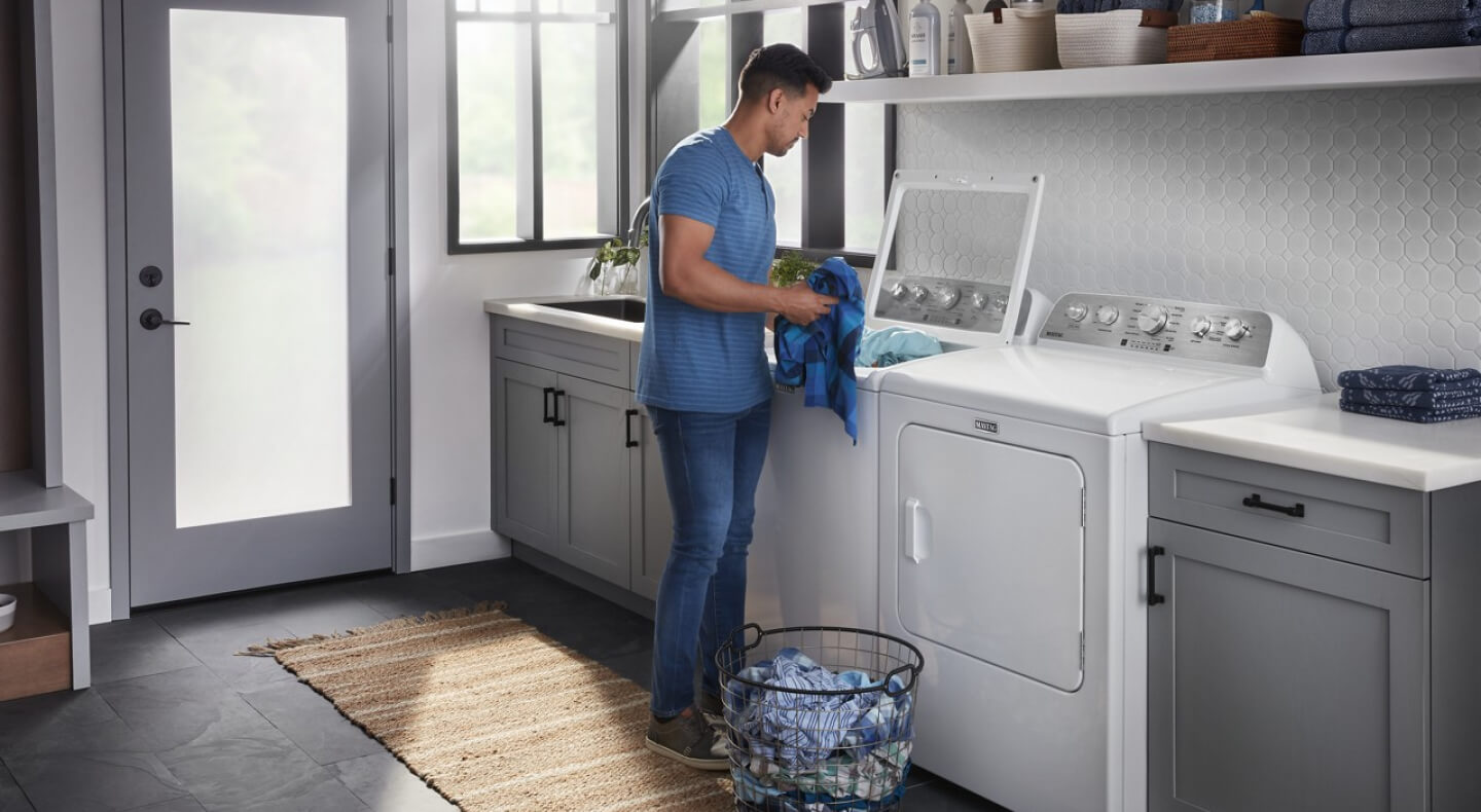 A person adding clothes to a Maytag® washer in a modern laundry room