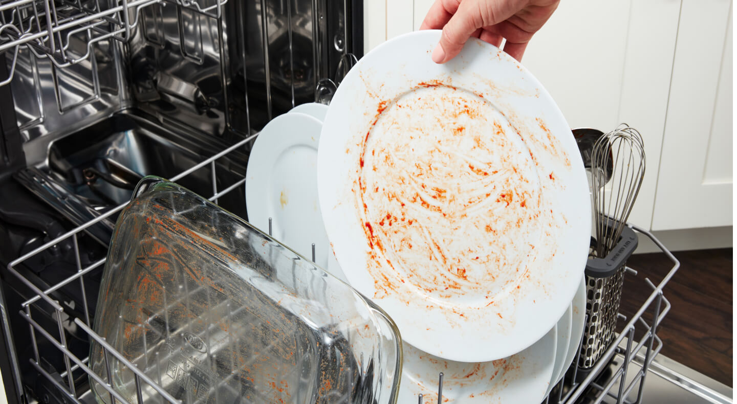 Person placing dirty dishes on dishwasher rack