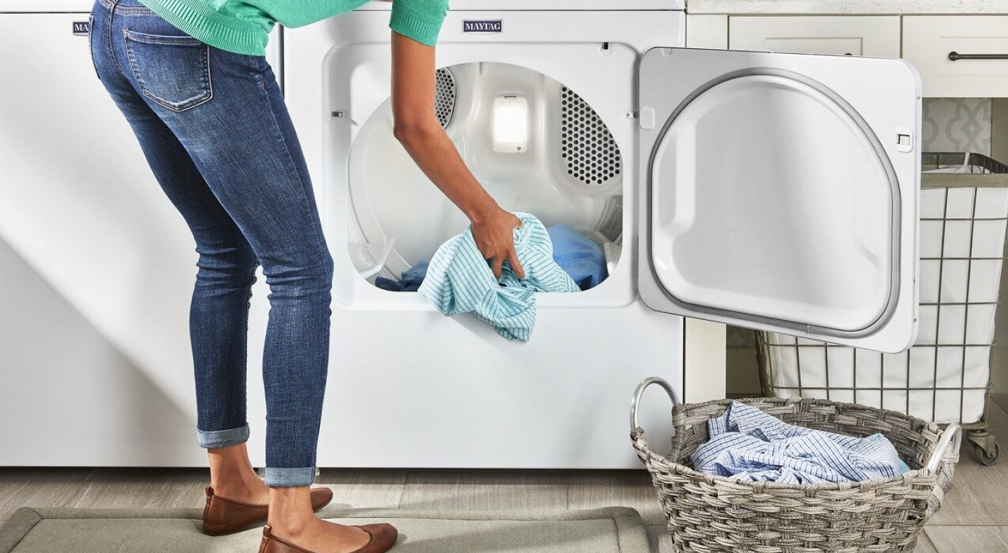 User adding clothes to white front load dryer