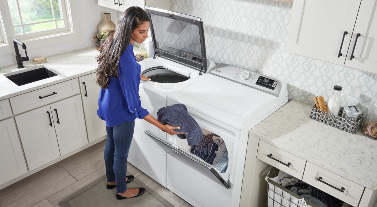 User transferring clothes from white top load washer to white front load dryer