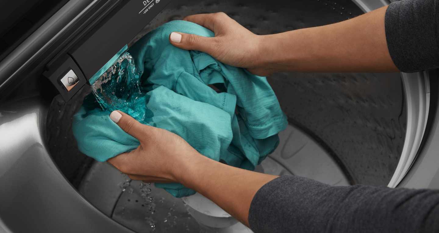 Person rinsing garment under water flow in Maytag® washing machine