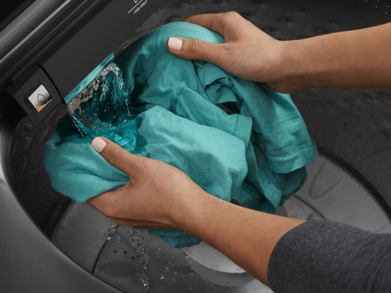 Person rinsing garment under water flow in Maytag® washing machine