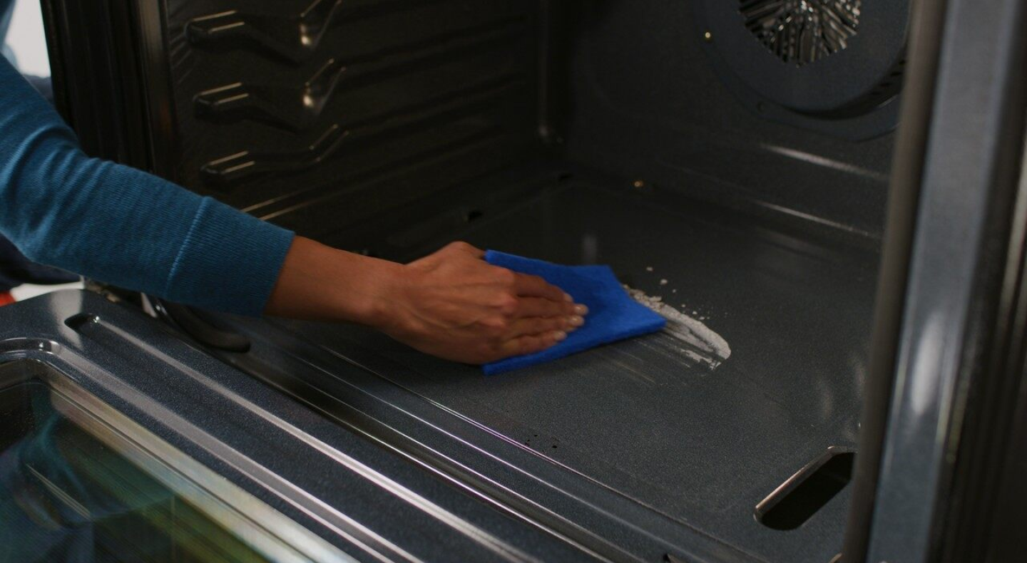 A person wipes down the bottom of an oven.
