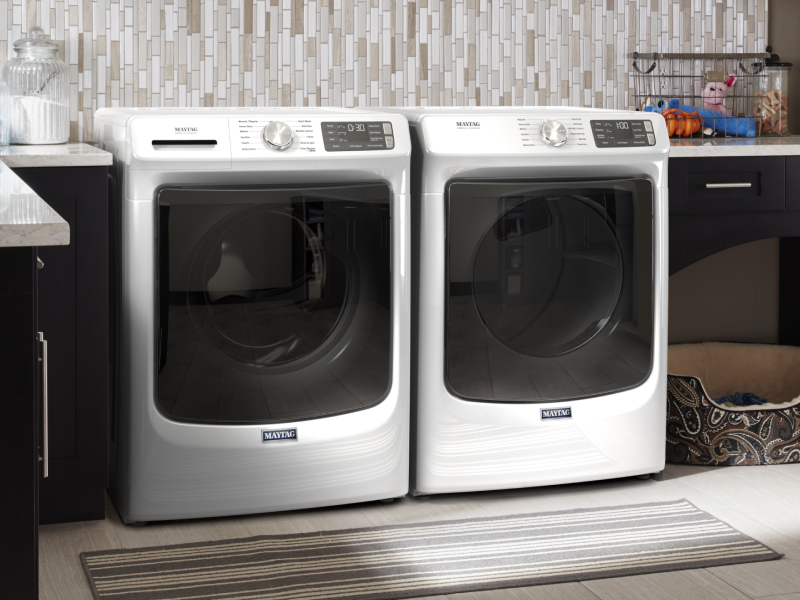 White Maytag® front load washer and dryer side by side in laundry room with dark cabinets