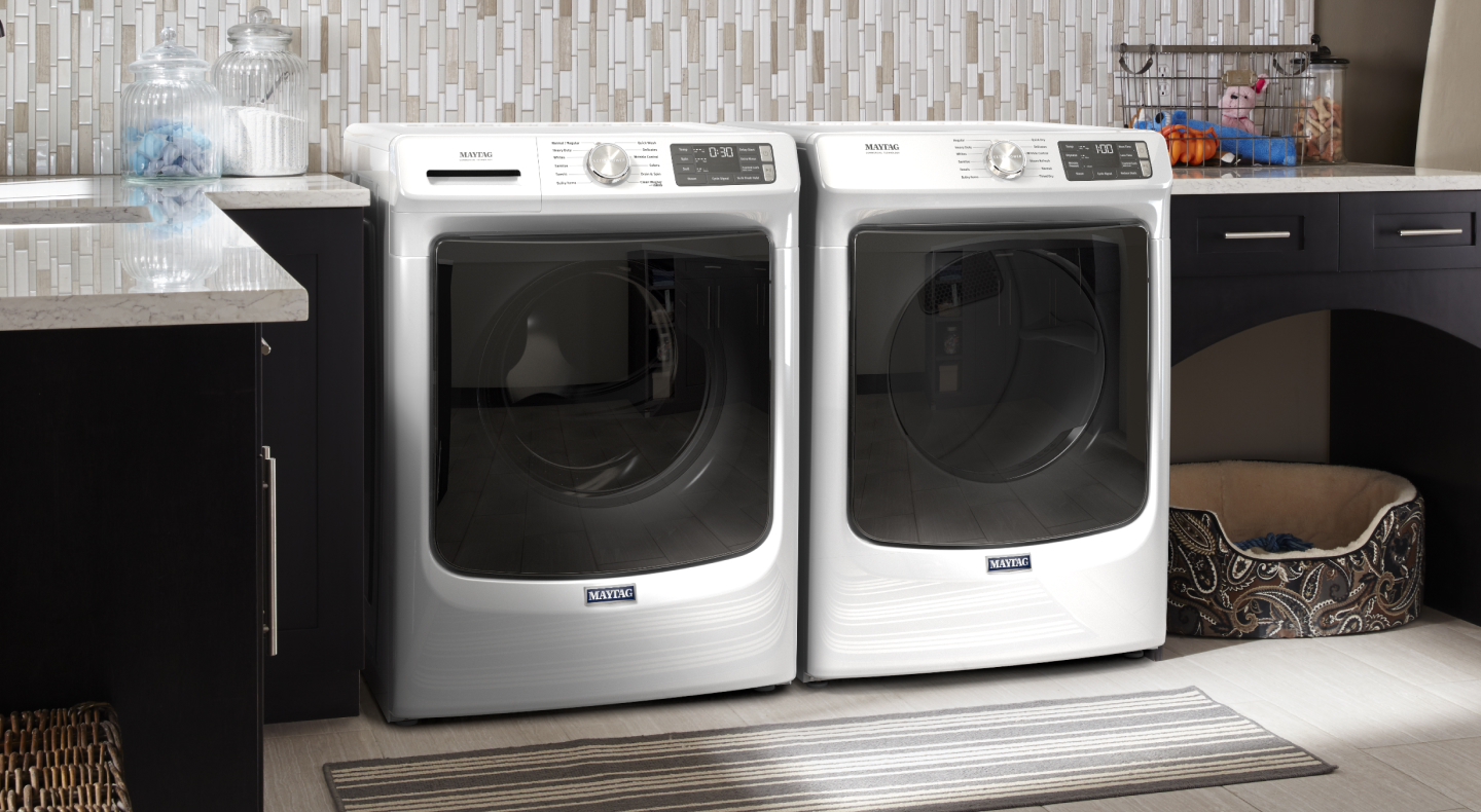 White Maytag® front load washer and dryer side by side in laundry room with dark cabinets