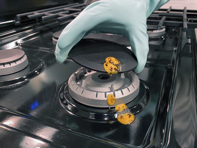 Hand removing the cap from a burner with cheese spilled on it