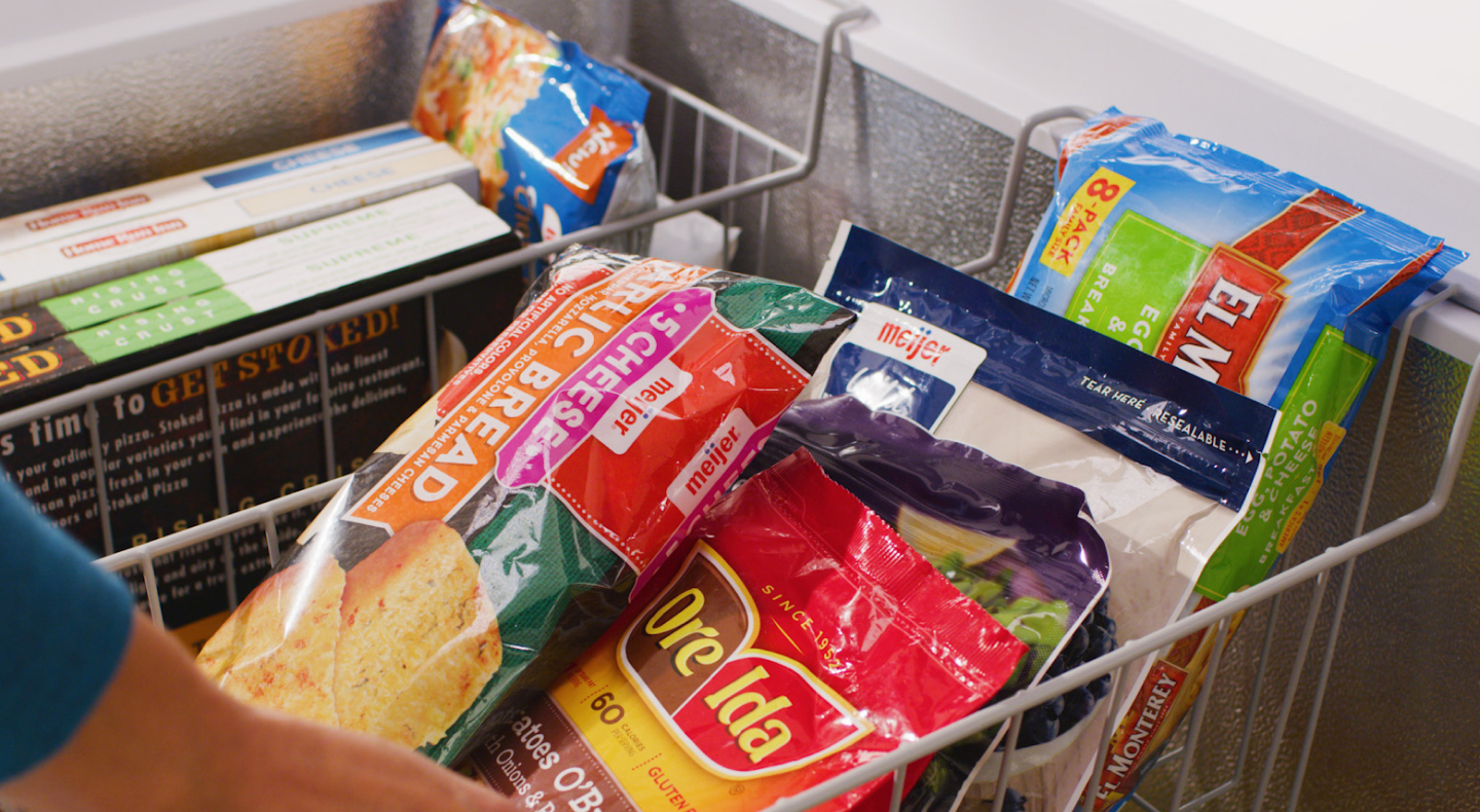 Person adjusting baskets filled with frozen food inside of chest freezer