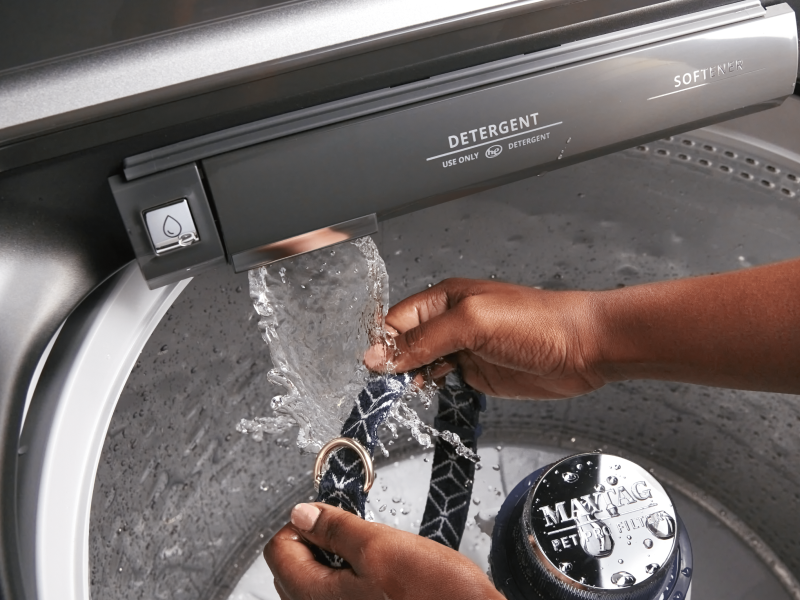 Person washing dog’s neck collar with Maytag® washer’s built-in faucet