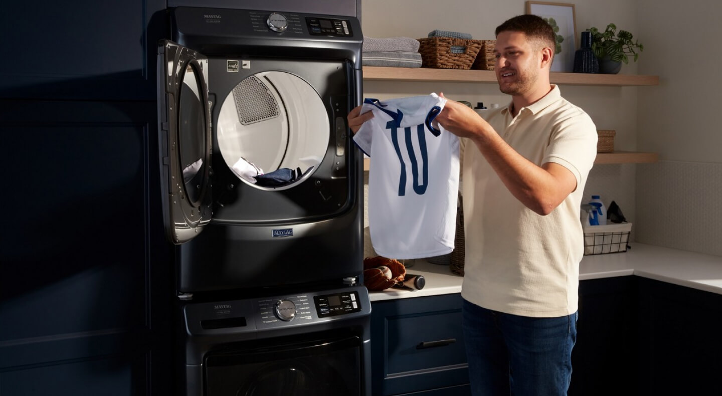 Person holding a jersey in front of a stackable washer and dryer