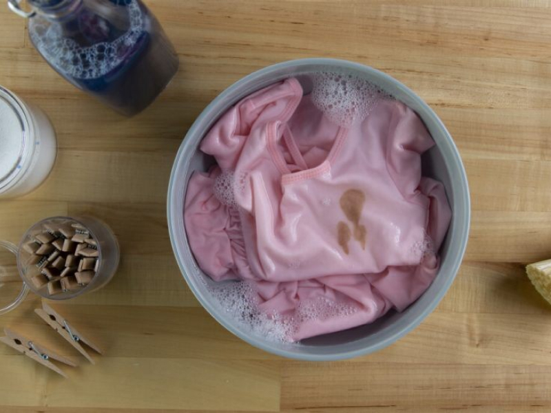 Stained pink blouse soaking in a bowl with cleaning products