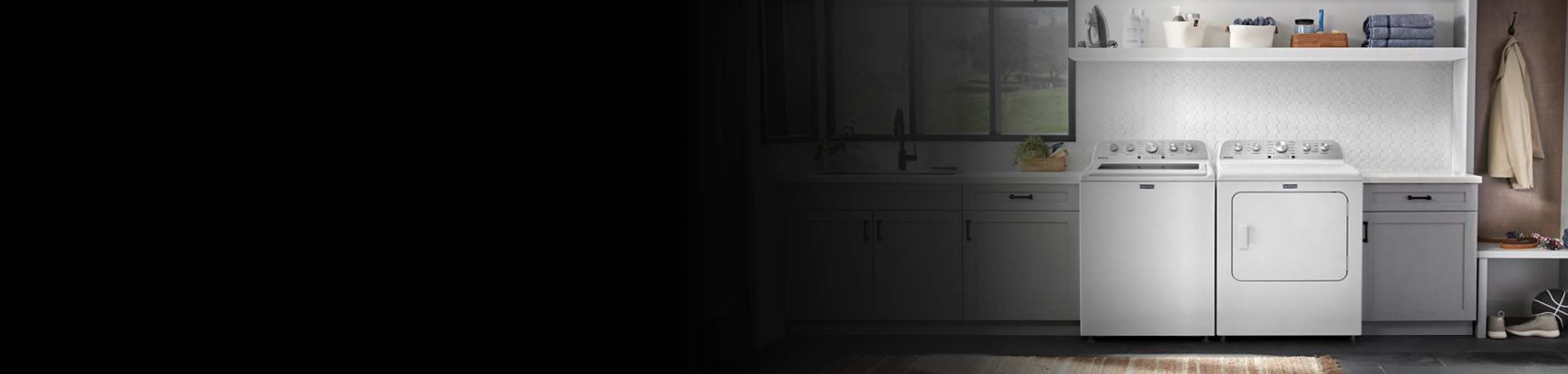 Overview of a laundry room with a top load washer, front load dryer, gray cabinets, and white backsplash tile.