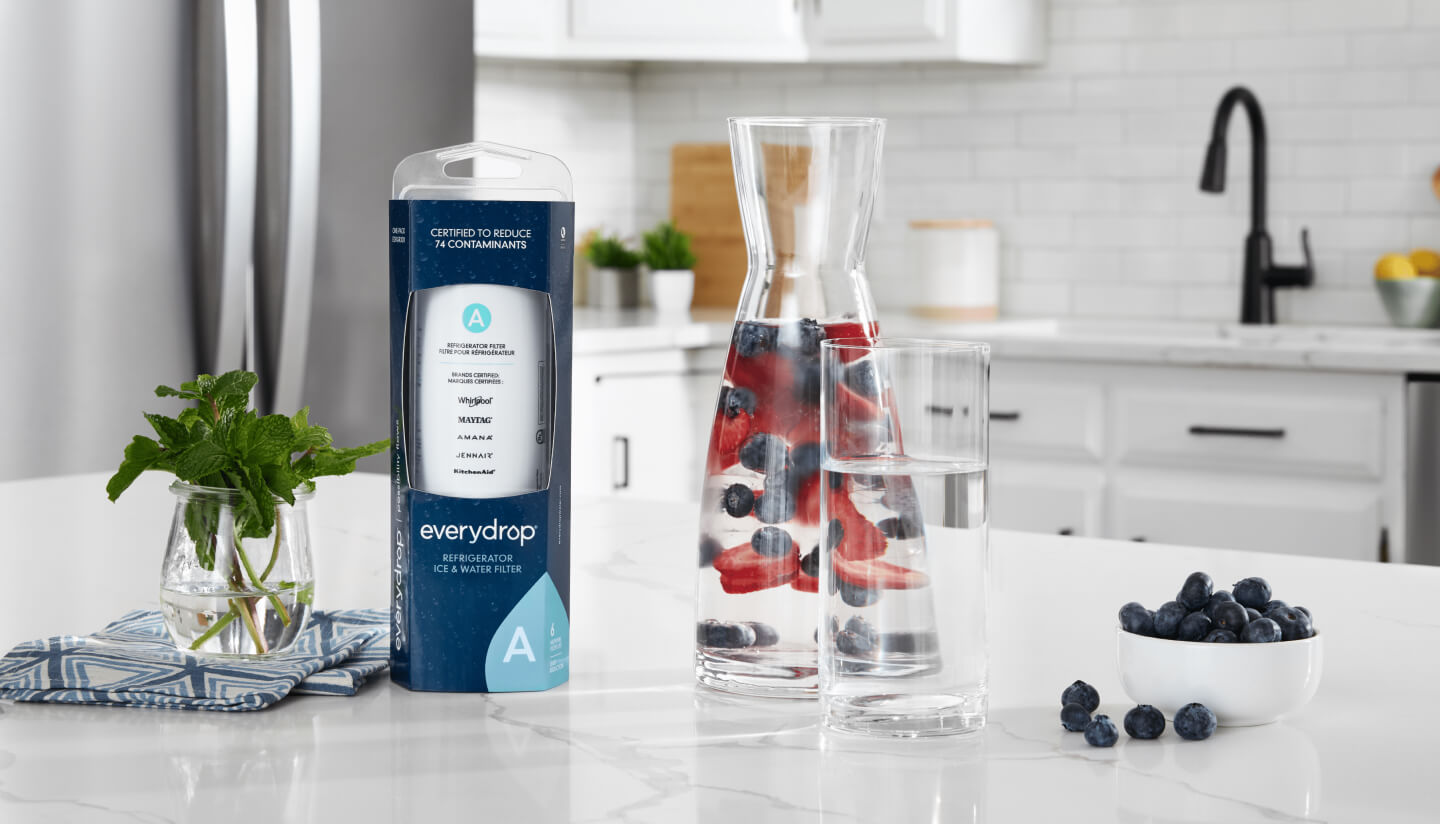 An everydrop® water filter on a kitchen counter next to a glass of water