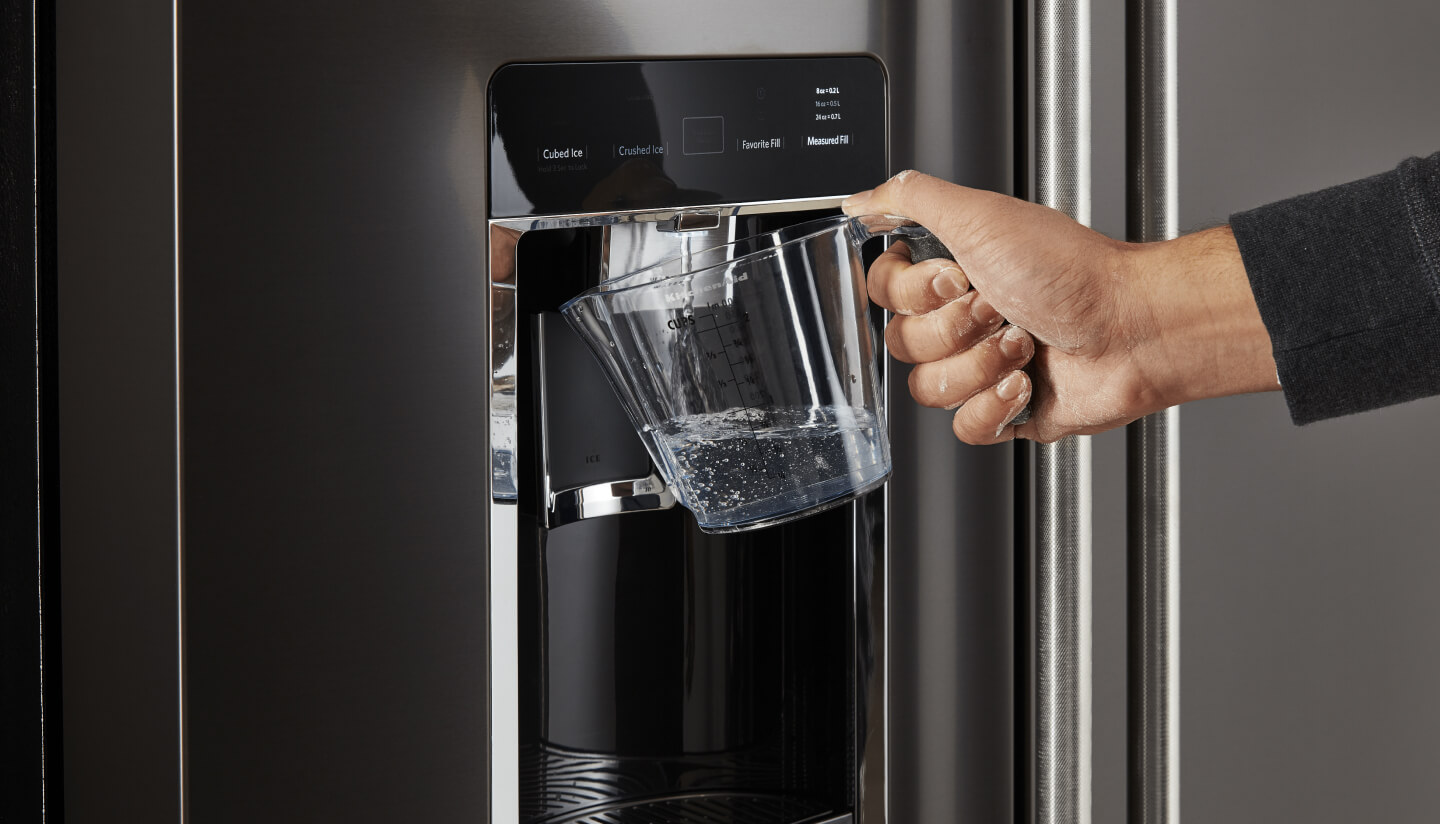 Person filling a large container with water from their refrigerator