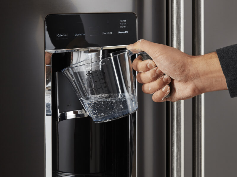 Person filling a large container with water from their refrigerator
