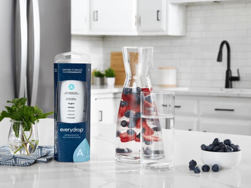 An everydrop® water filter on a kitchen counter next to a glass of water