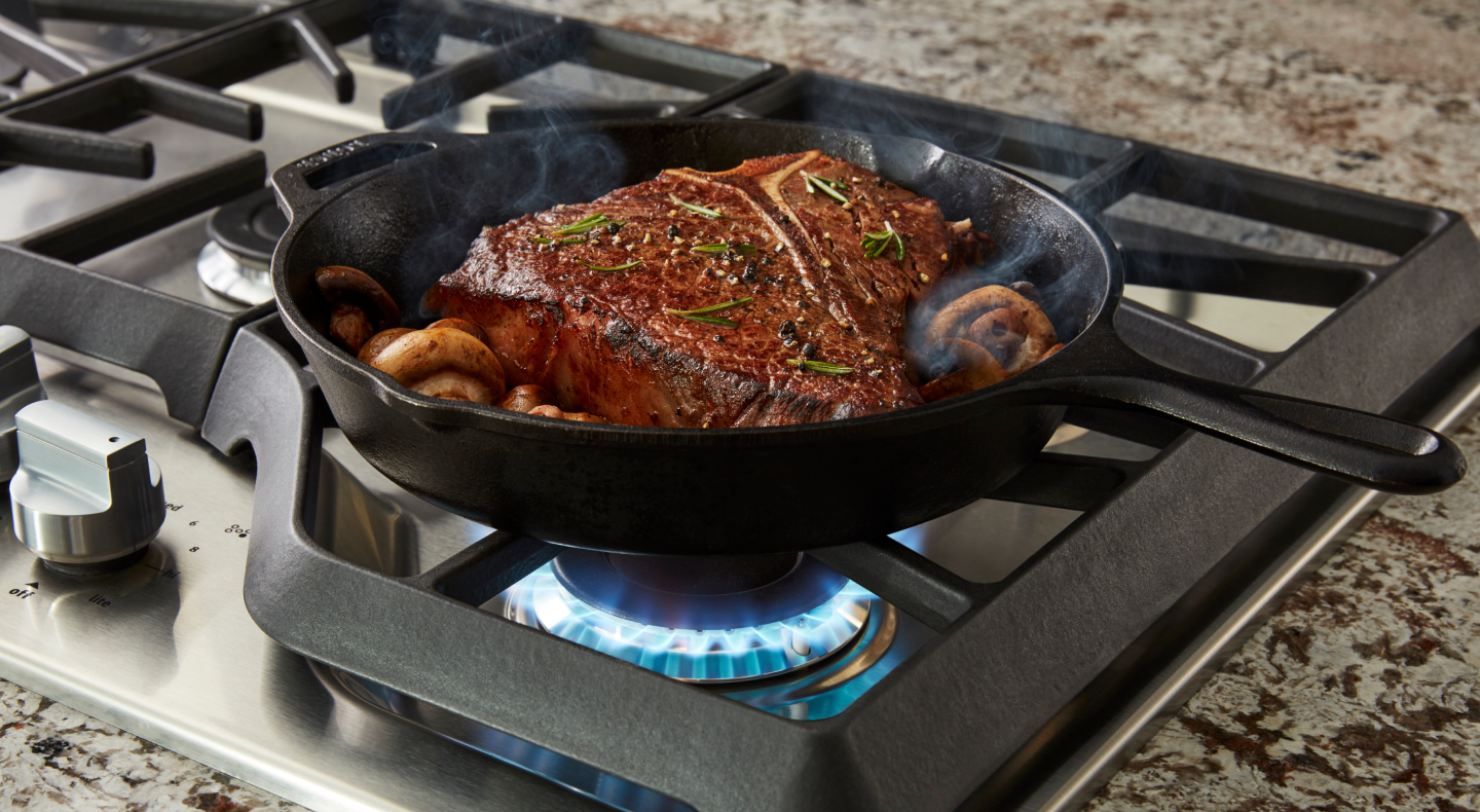 A closeup of meat and veggies sautéing on the cooktop of a Maytag® gas cooktop