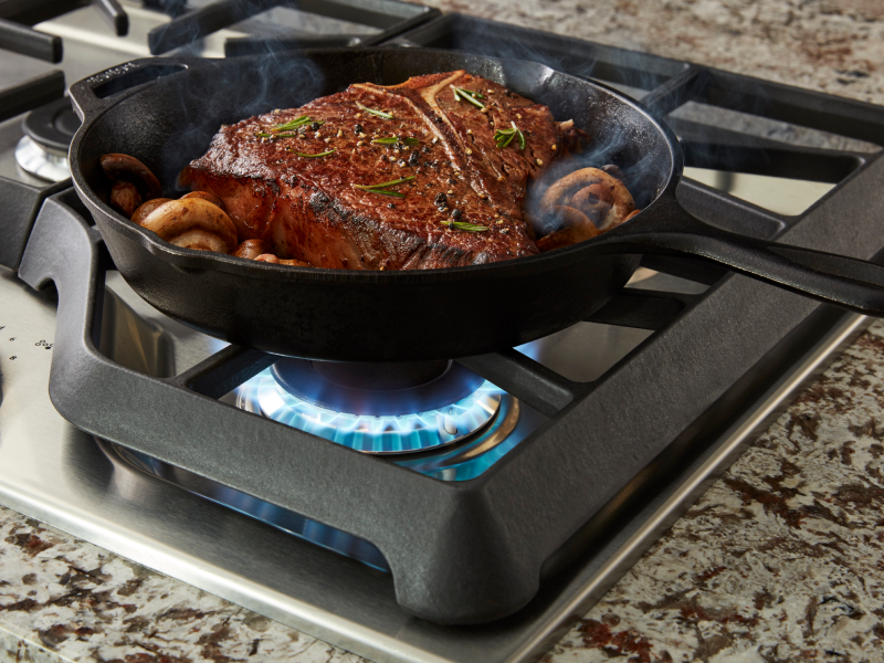 A closeup of meat and veggies sautéing on the cooktop of a Maytag® gas cooktop