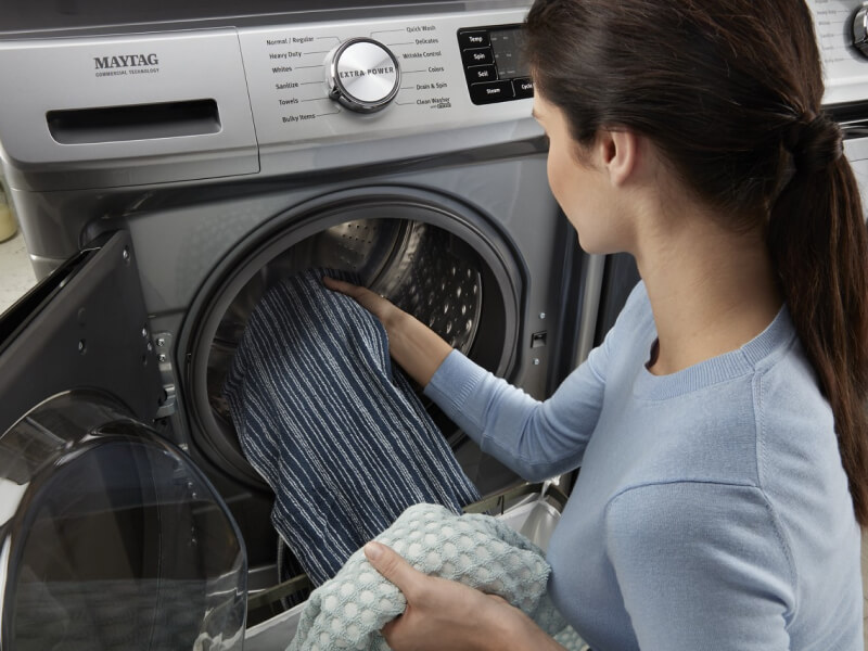 A person adding laundry to a Maytag® front load washer