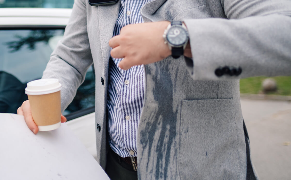 Person holding a coffee cup with a spill on their suit