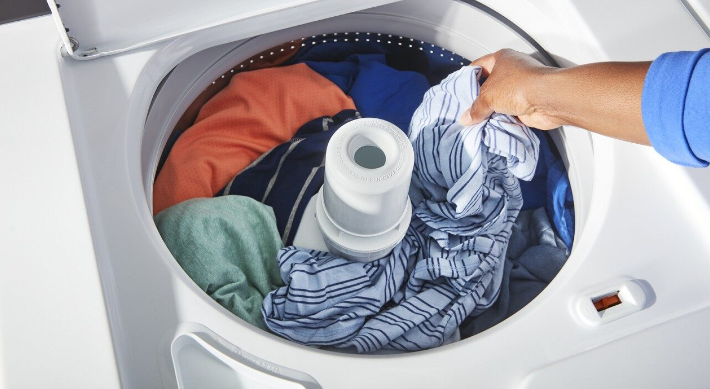 A woman adding laundry to a Maytag® top load washing machine.