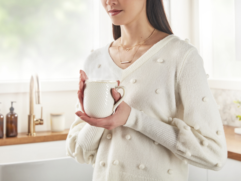 A person wearing a hand-knitted shirt, holding a mug