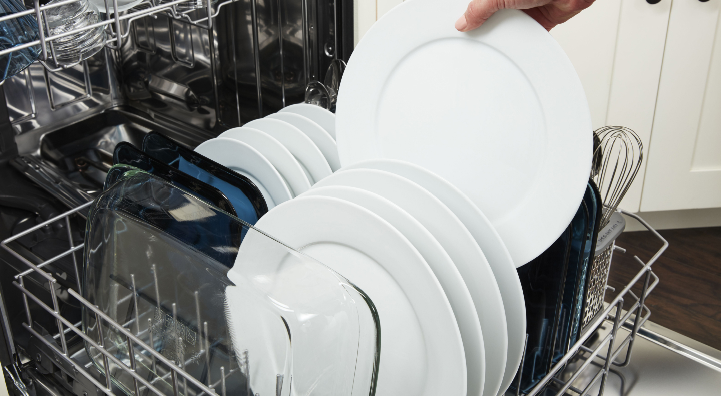 A person unloading a clean dish from a dishwasher rack 