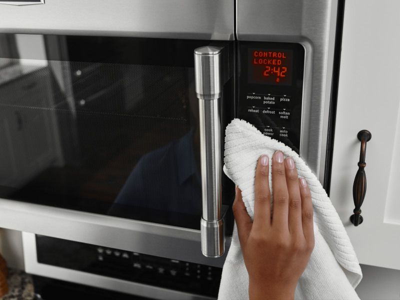 Hand holding white towel wiping microwave control panel