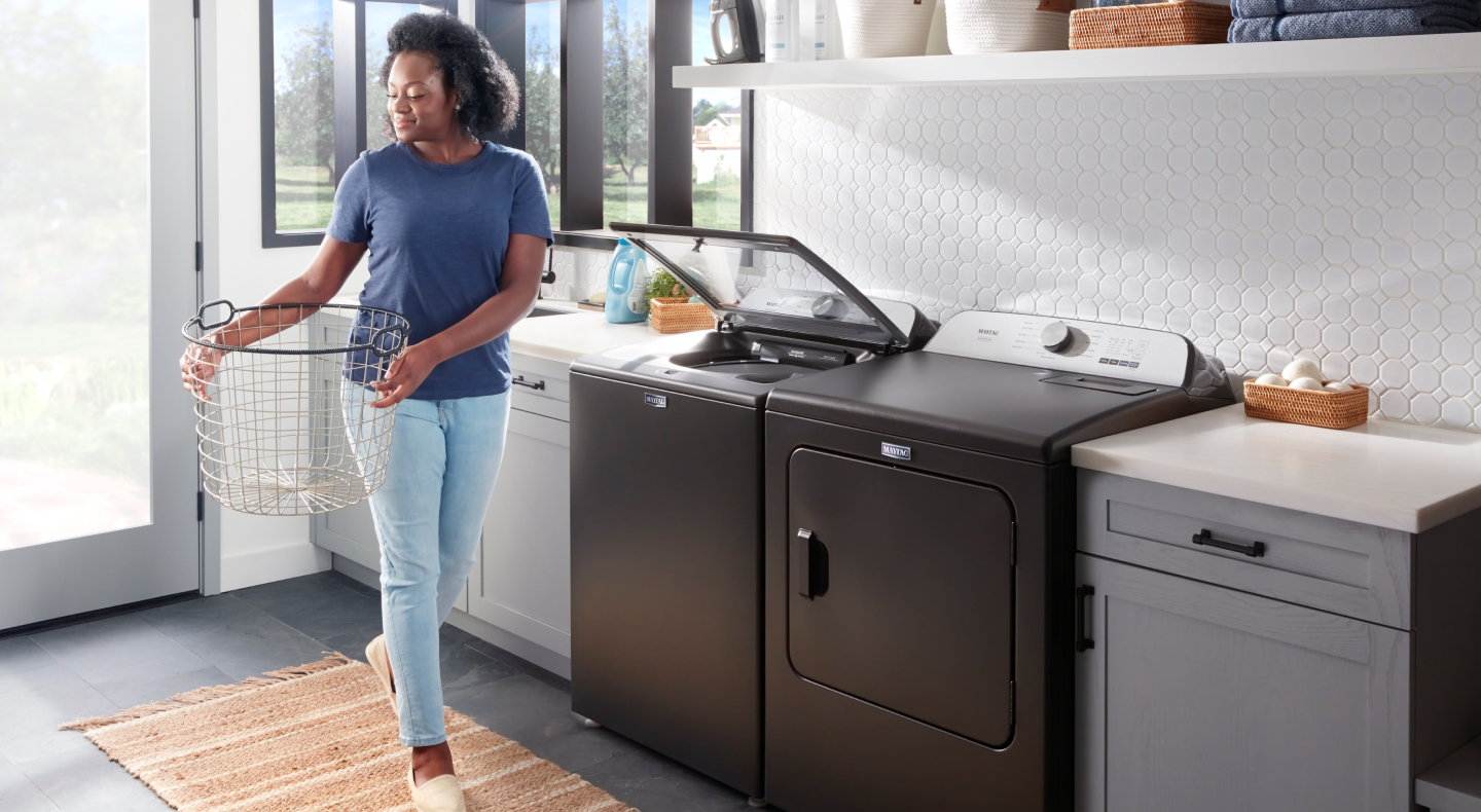 Person carrying a laundry basket next to a washing machine