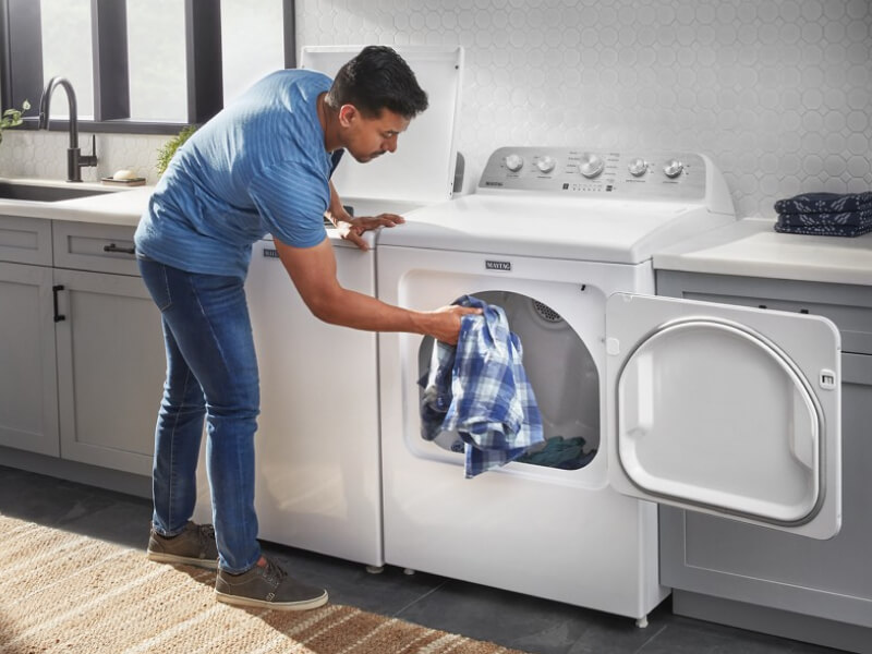 A person adding a blue and white shirt to a dryer