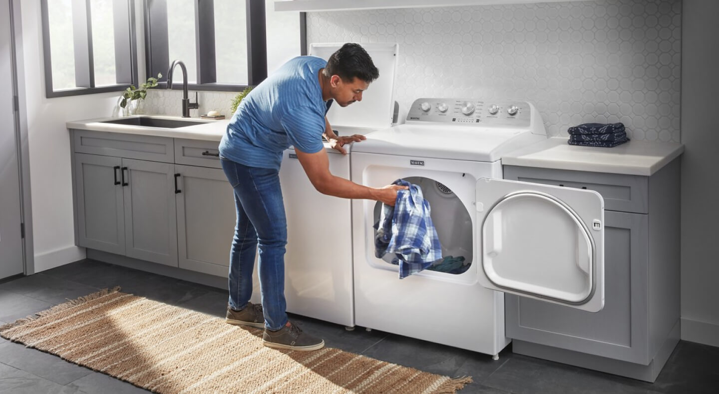 A person adding a blue and white shirt to a dryer
