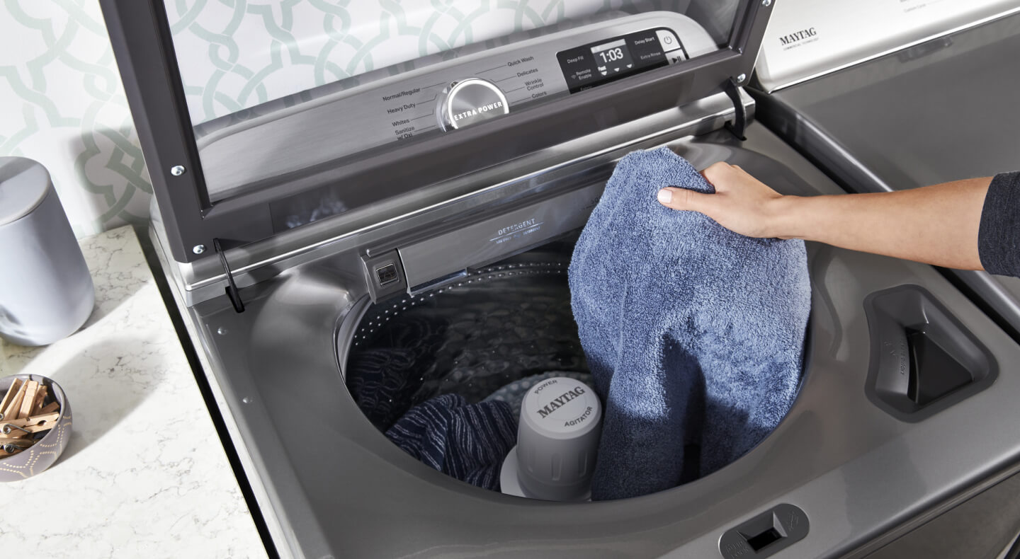 A person adding towels to a Maytag® top load washer