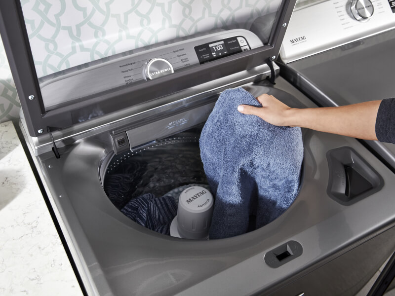 A person adding towels to a Maytag® top load washer