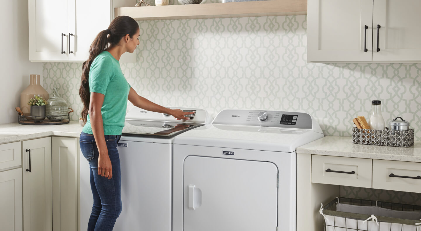 A person selecting a wash cycle on a Maytag® top load washer in a modern laundry room