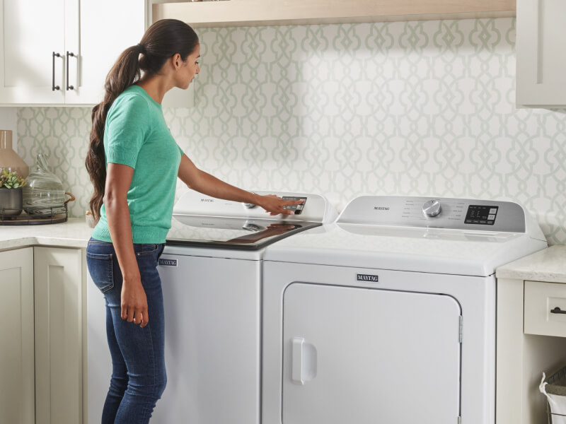 A person selecting a wash cycle on a Maytag® top load washer in modern laundry room