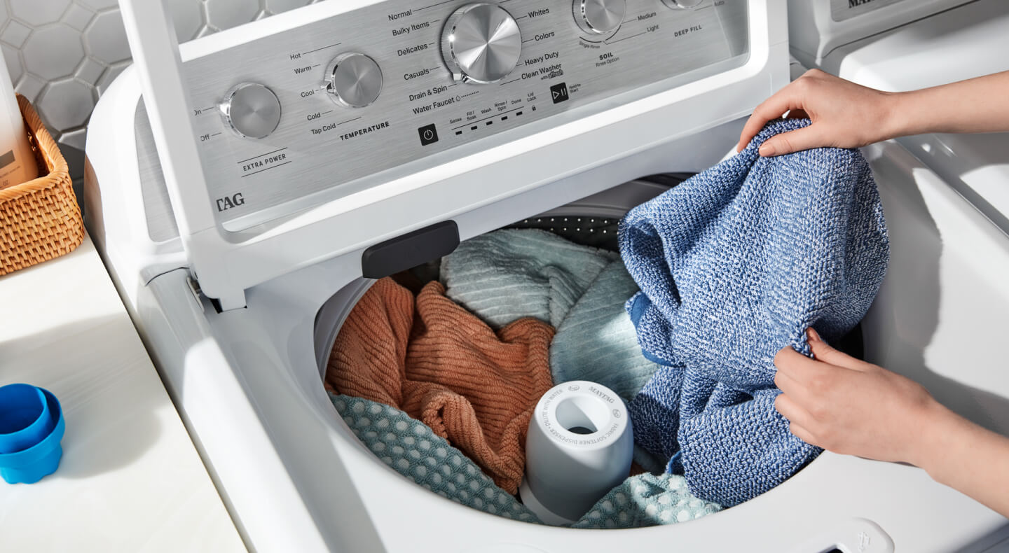 A closeup of a person adding laundry items to a Maytag® top load washer