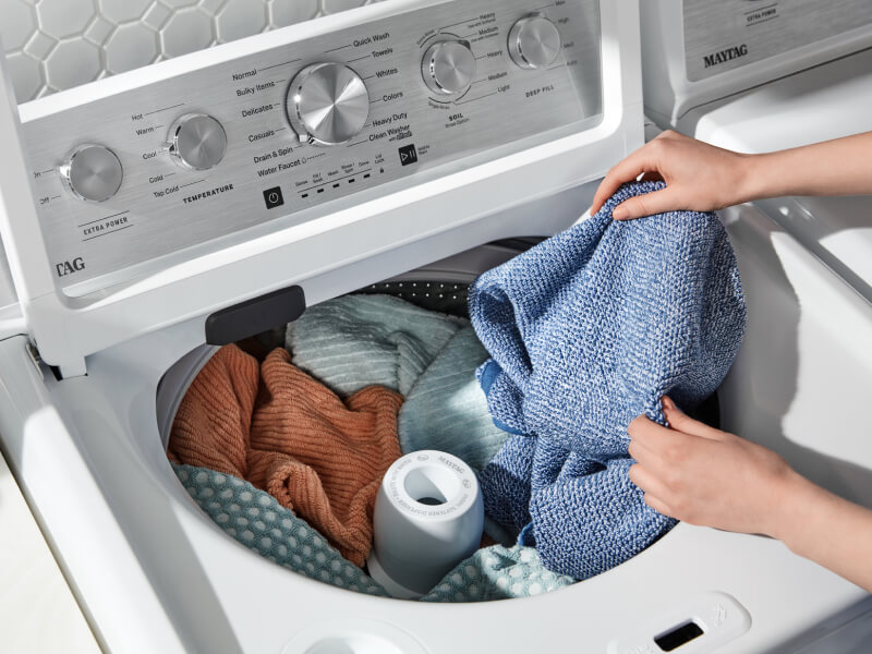 A closeup of a person adding laundry items to a Maytag® top load washer