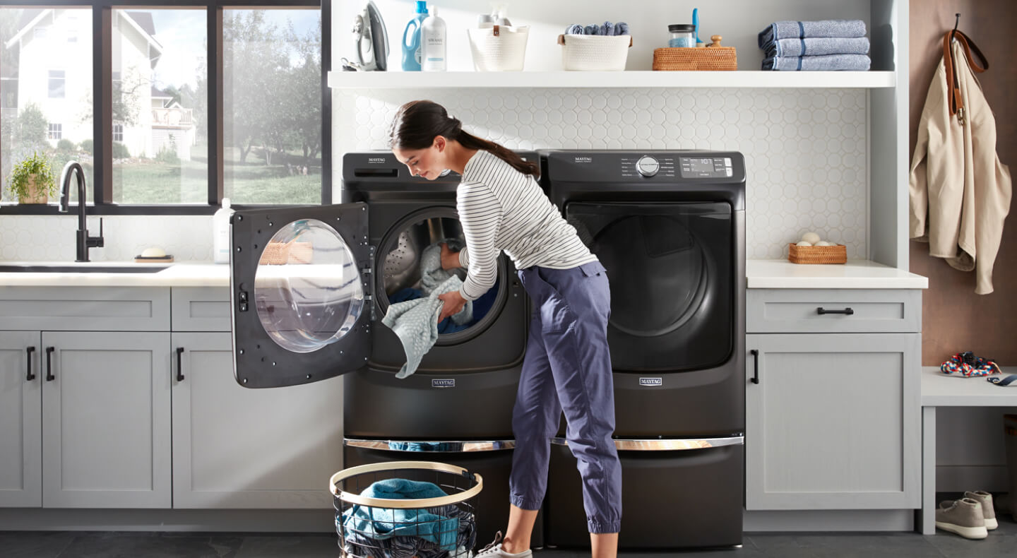 A person adding laundry items to a Maytag® front load washer in modern laundry room