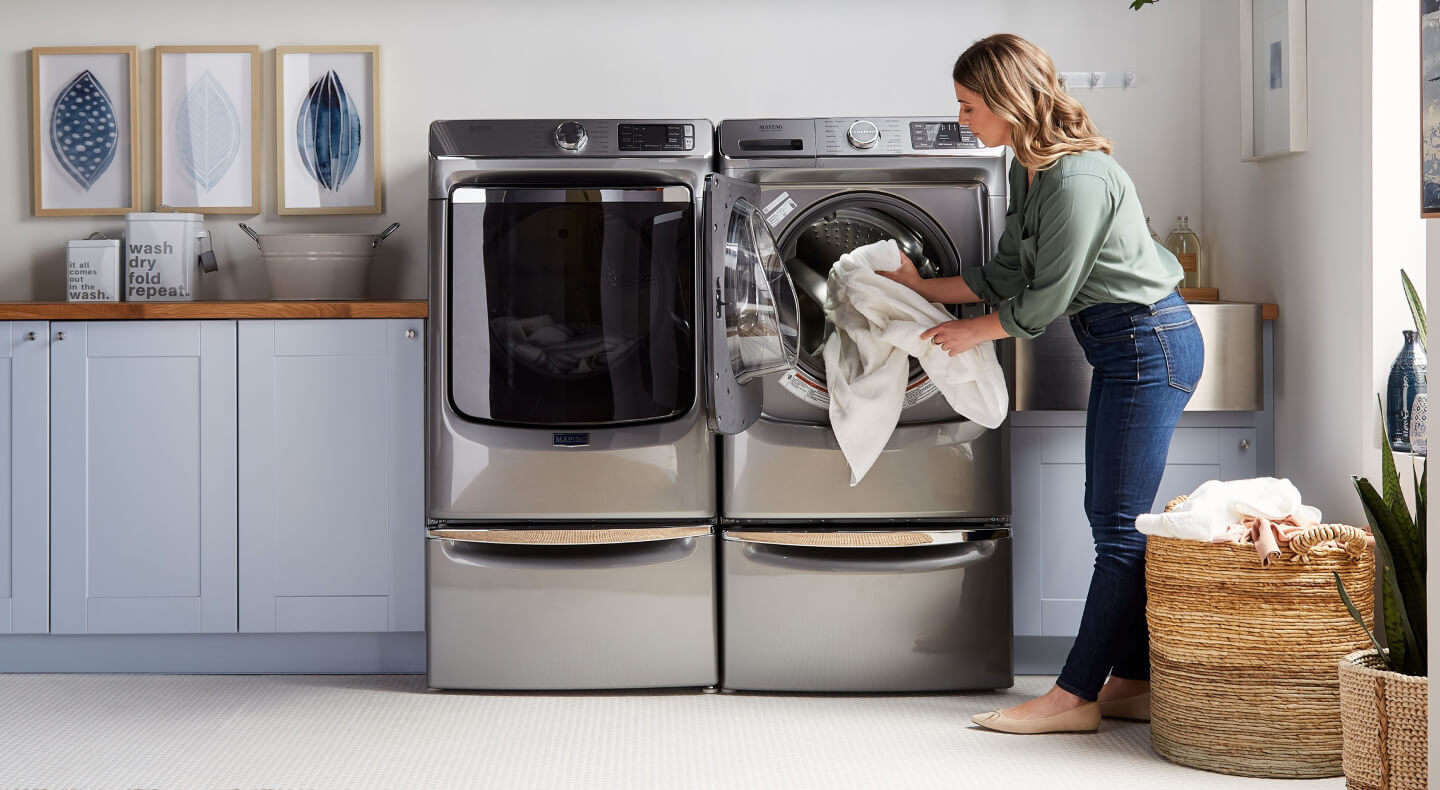 A person adding laundry items to a Maytag® dryer in modern laundry room