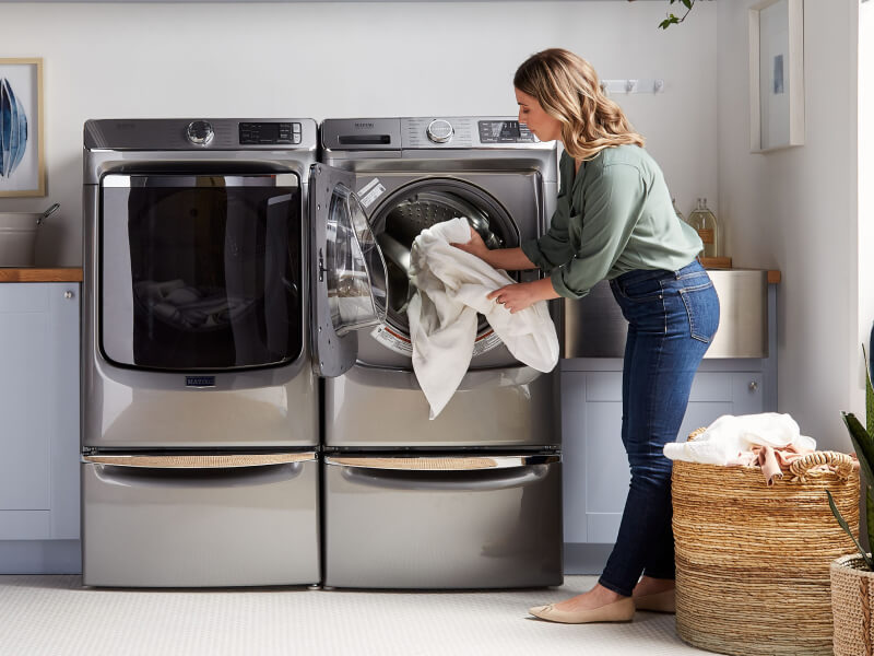 A person adding laundry items to a Maytag® dryer in modern laundry room