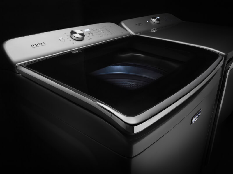 Maytag® stainless steel top load washing machine against a black background
